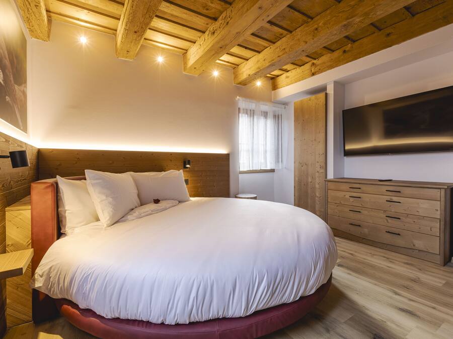 Quarto com uma cama grande, cabeceira de madeira, cômoda e televisão na parede.
