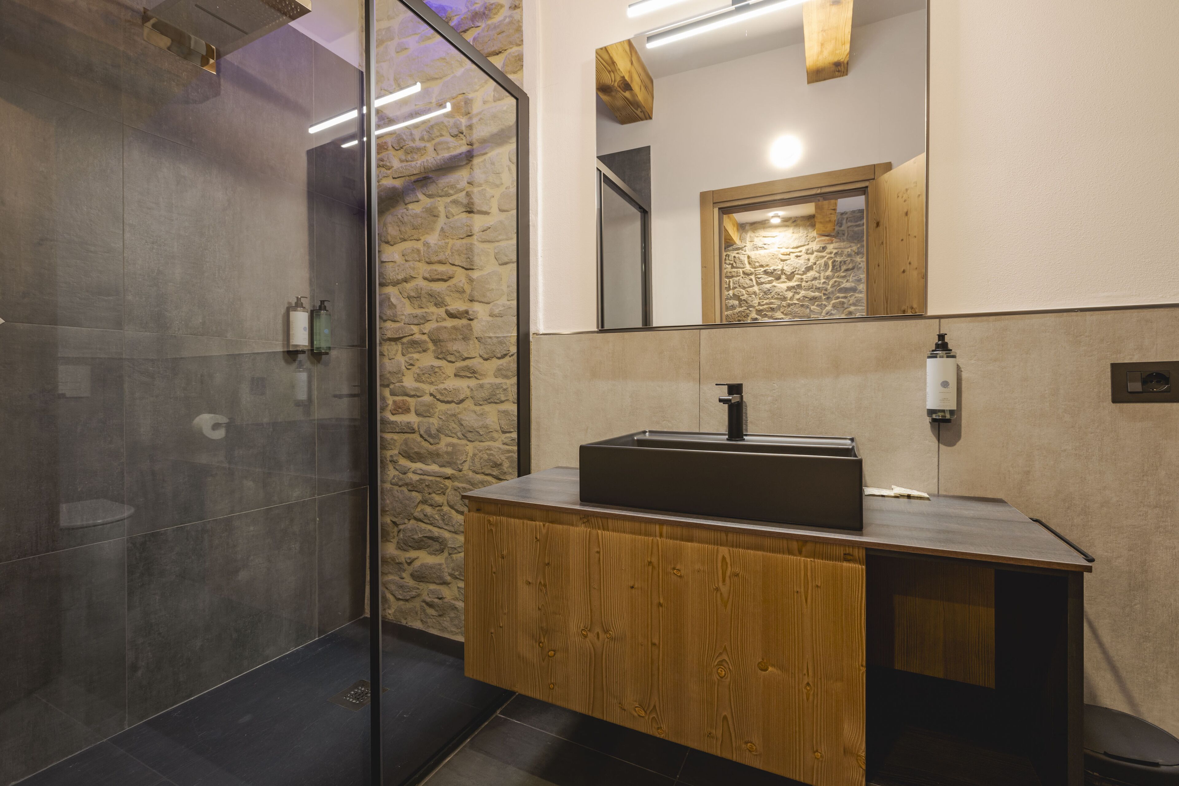 A modern bathroom with a glass shower enclosure, a wooden vanity with a sink, and a stone accent wall.