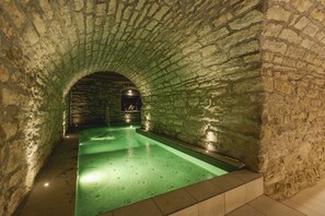 A stone-walled pool area with a green pool, stone flooring, and a stone archway. - Granduca Mountain Wellness Apartments Campigna (Santa Sofia)