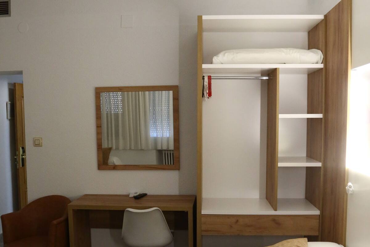 A compact hotel room with a bunk bed, a desk with a chair, a small wardrobe, and a bedside table.
