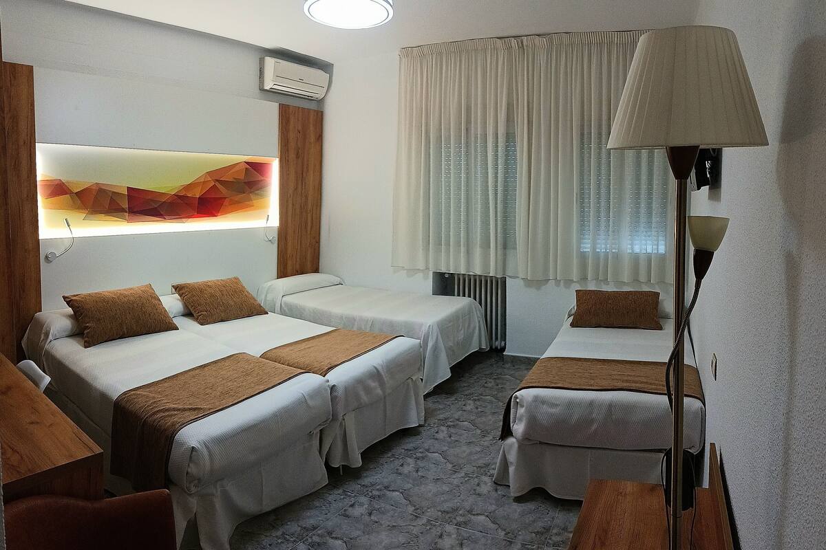 A hotel room with two single beds, a sofa, a standing lamp, and a large window with curtains.