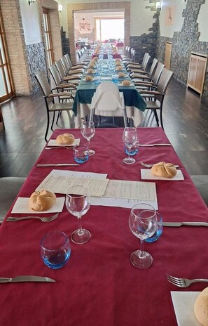 A long dining table set with red tablecloths, multiple chairs, and wine glasses. - Hostal Real (Plasencia)