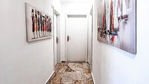 Um corredor com piso de mármore, paredes brancas e duas pinturas nas paredes.