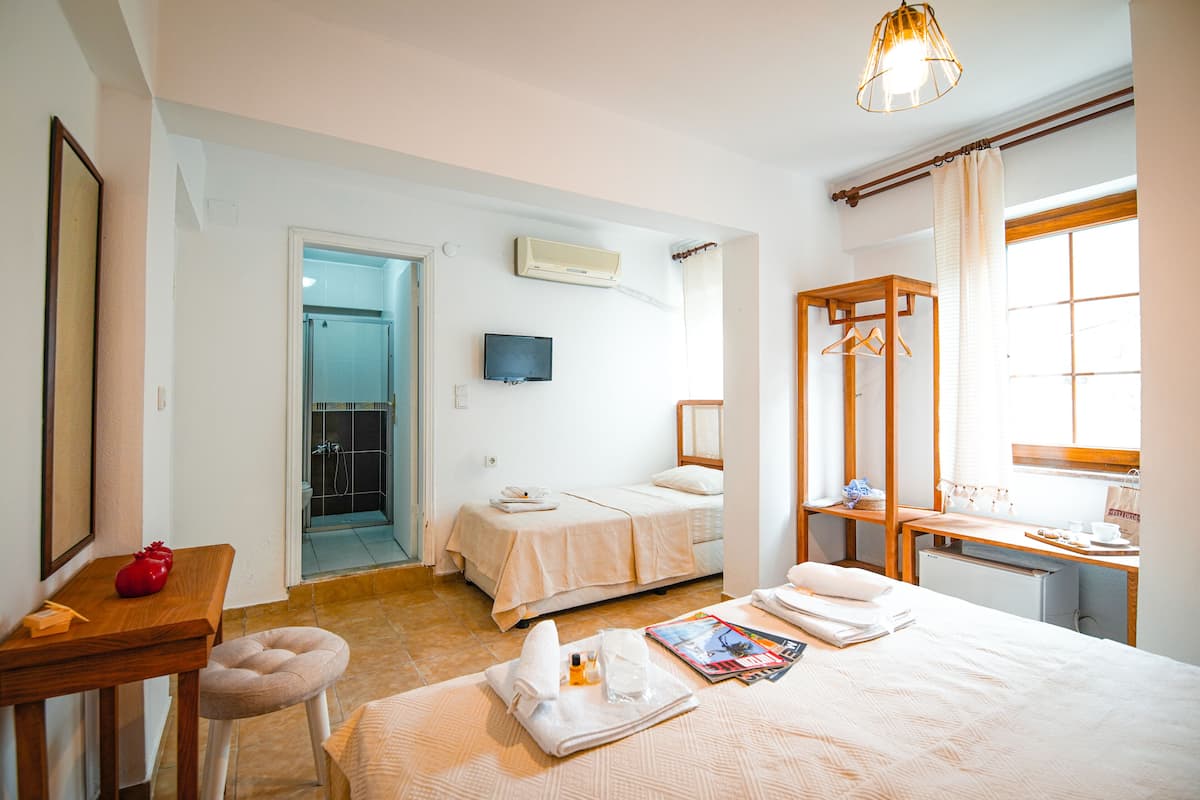 Habitación de hotel con dos camas, un escritorio, una silla, un televisor y un baño visible a través de una puerta abierta.