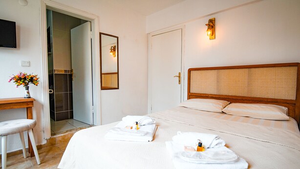 Quarto de hotel com uma cama, uma mesa de escritório e um banheiro visível através de uma porta aberta.