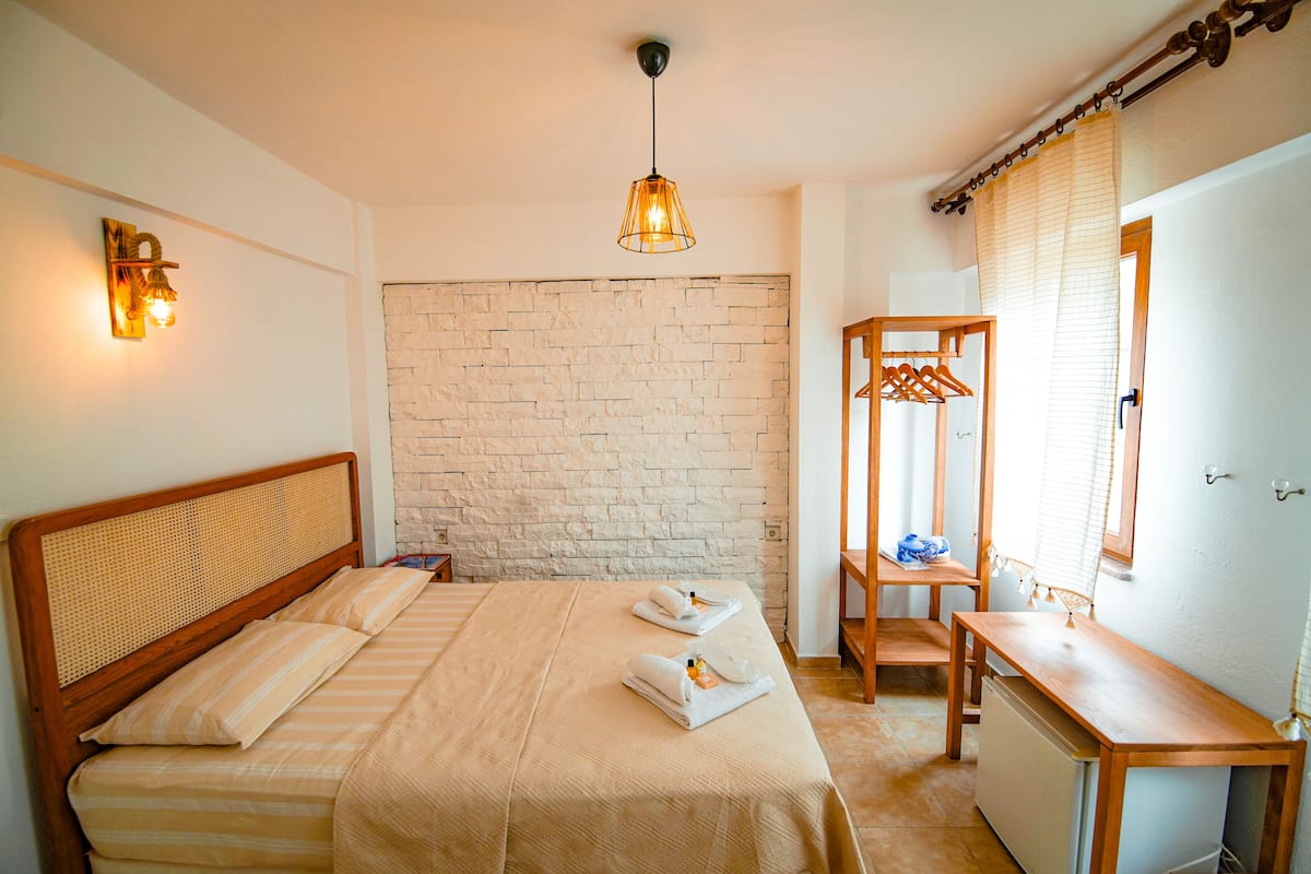 Un dormitorio con cama, mesitas de noche, un escritorio de madera, una lámpara colgante y una pared de piedra.