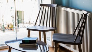 Ein Zimmer mit Holzboden, einem Glastisch mit Büchern, einem schwarzen Stuhl und einer Heizung.