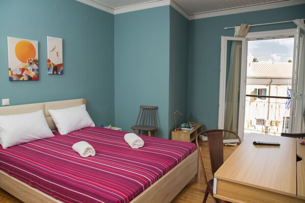 A bedroom with a bed, a desk, a chair, and a window with a view of buildings.