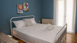Ein Schlafzimmer mit einem Bett, weißer Bettwäsche, einem Kopfkissen mit dem Schriftzug „HOME“ sowie einem Heizkörper und einem Fenster mit Vorhängen.