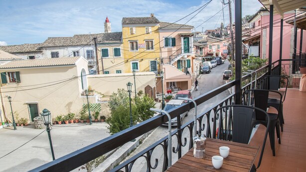 Ein Balkon mit Holztisch und Stühlen, mit Blick auf eine Straße mit bunten Gebäuden und geparkten Autos.