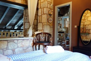 A room with a stone wall, a wooden chair, a bed with a blue and white patterned bedspread, and a mirror on the wall.