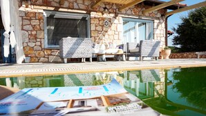 A stone building with a pool, wicker furniture, and a magazine on the table. - Ariadne Eco Retreat (Polygyros)