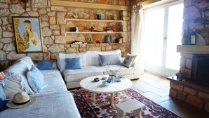 A cozy living room with a stone wall, a white sofa, a patterned rug, and a fireplace. - Ariadne Eco Retreat (Polygyros)