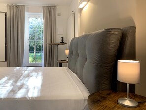 A hotel room with a large bed, a bedside table with a lamp, a view of greenery through the window, and a door with curtains. - B&B Villa Paradiso (Urbino)