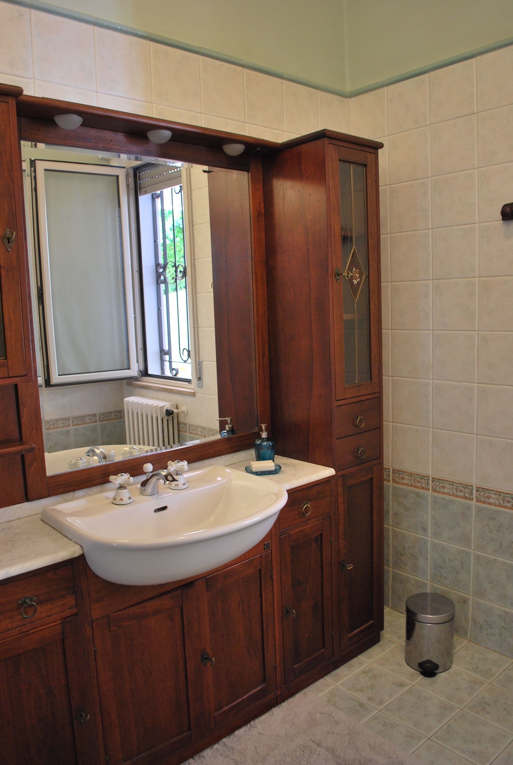 Ein Badezimmer mit Holzwaschtisch, einem großen Spiegel, einem weißen Waschbecken und einem Heizkörper.