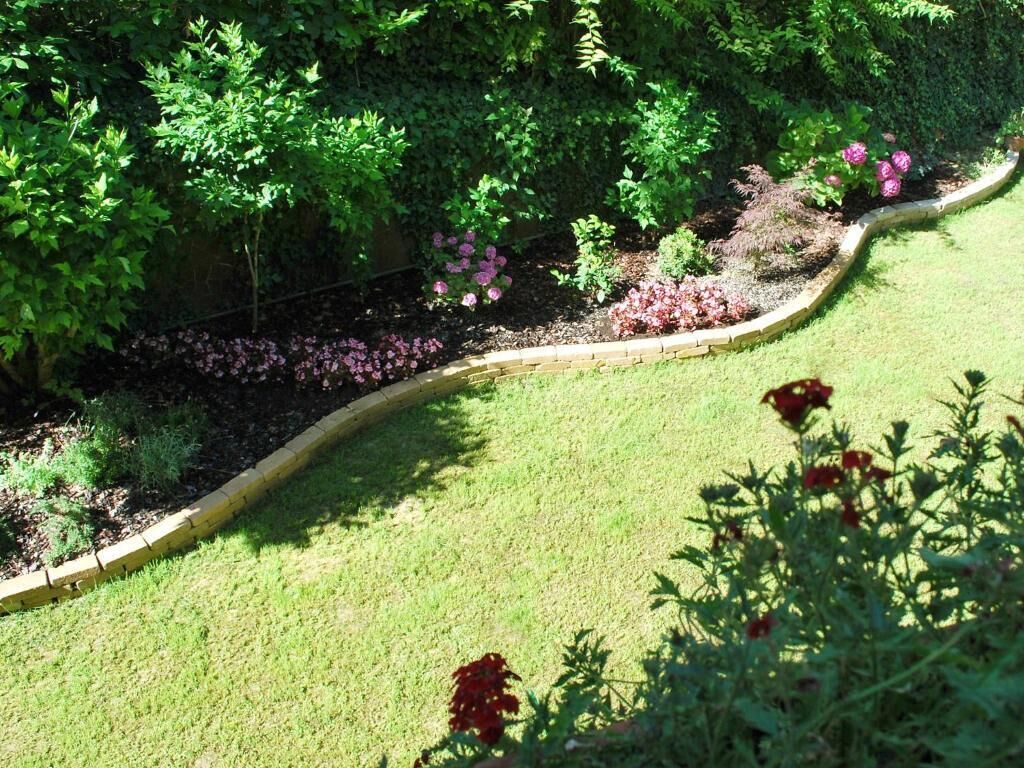 A landscaped garden with a curved brick border, various shrubs, and flowering plants.