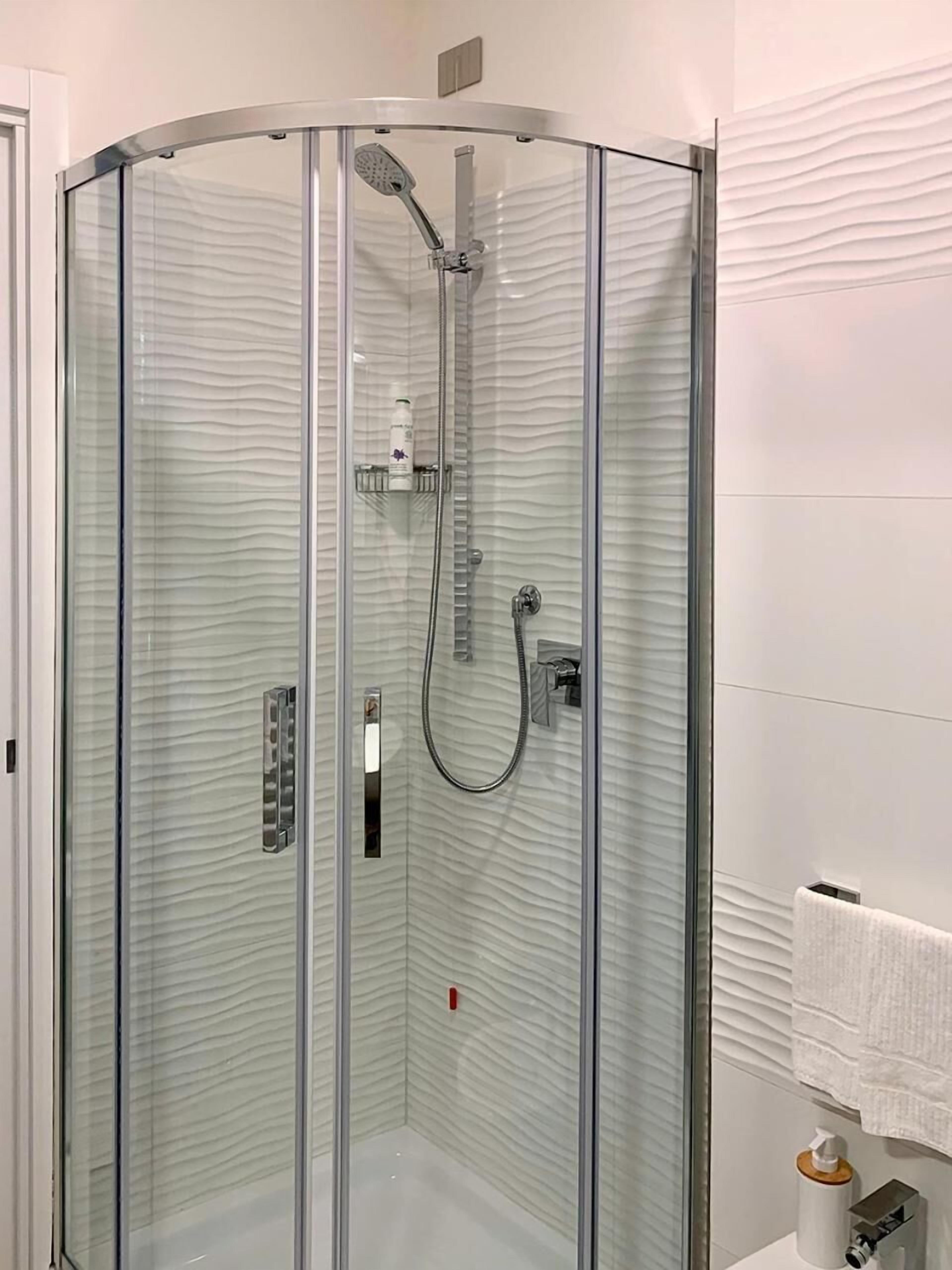 Cabina de ducha con paredes de vidrio, cabezal de ducha de mano y grifo empotrado.