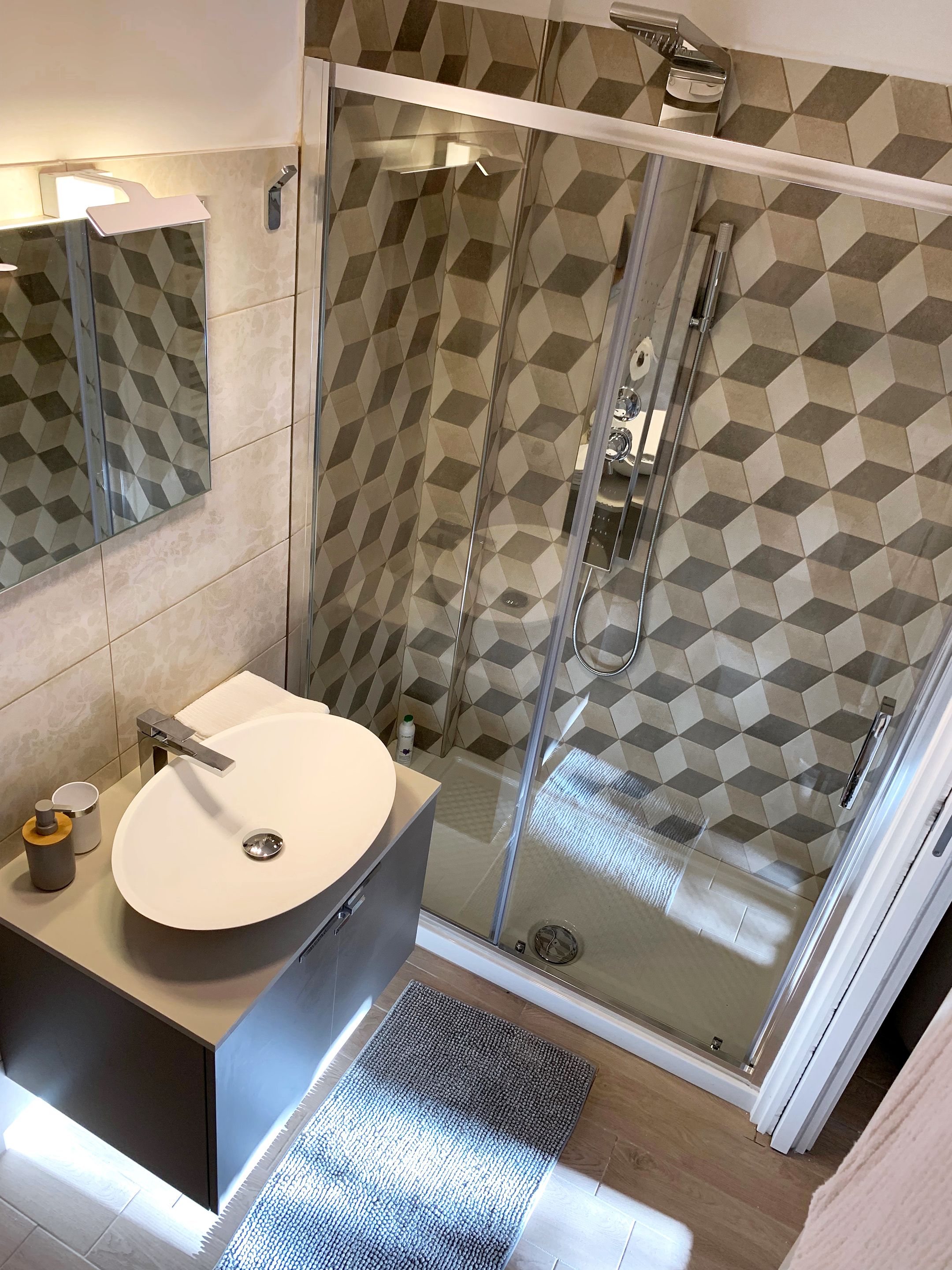 A modern bathroom with a glass-enclosed shower, a round sink, and a geometric-patterned tile backsplash.