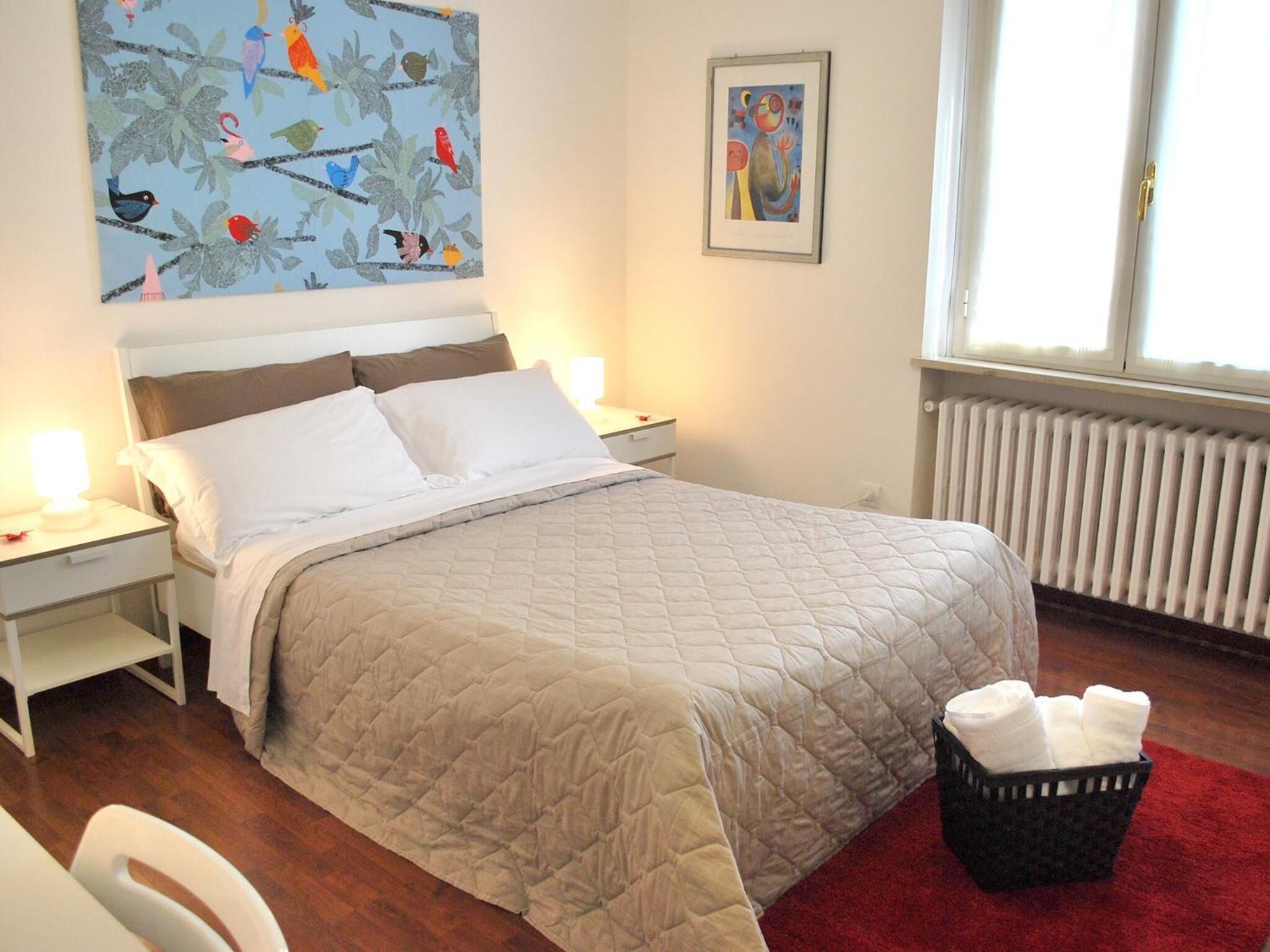 Ein ordentlich eingerichtetes Schlafzimmer mit Bett, Nachttischen, einem Heizkörper und einem Fenster mit Vorhängen.
