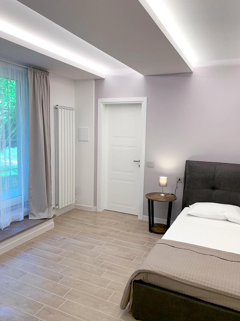 Una habitación de hotel con una cama, una mesita de noche con lámpara, una ventana con cortinas y un radiador.