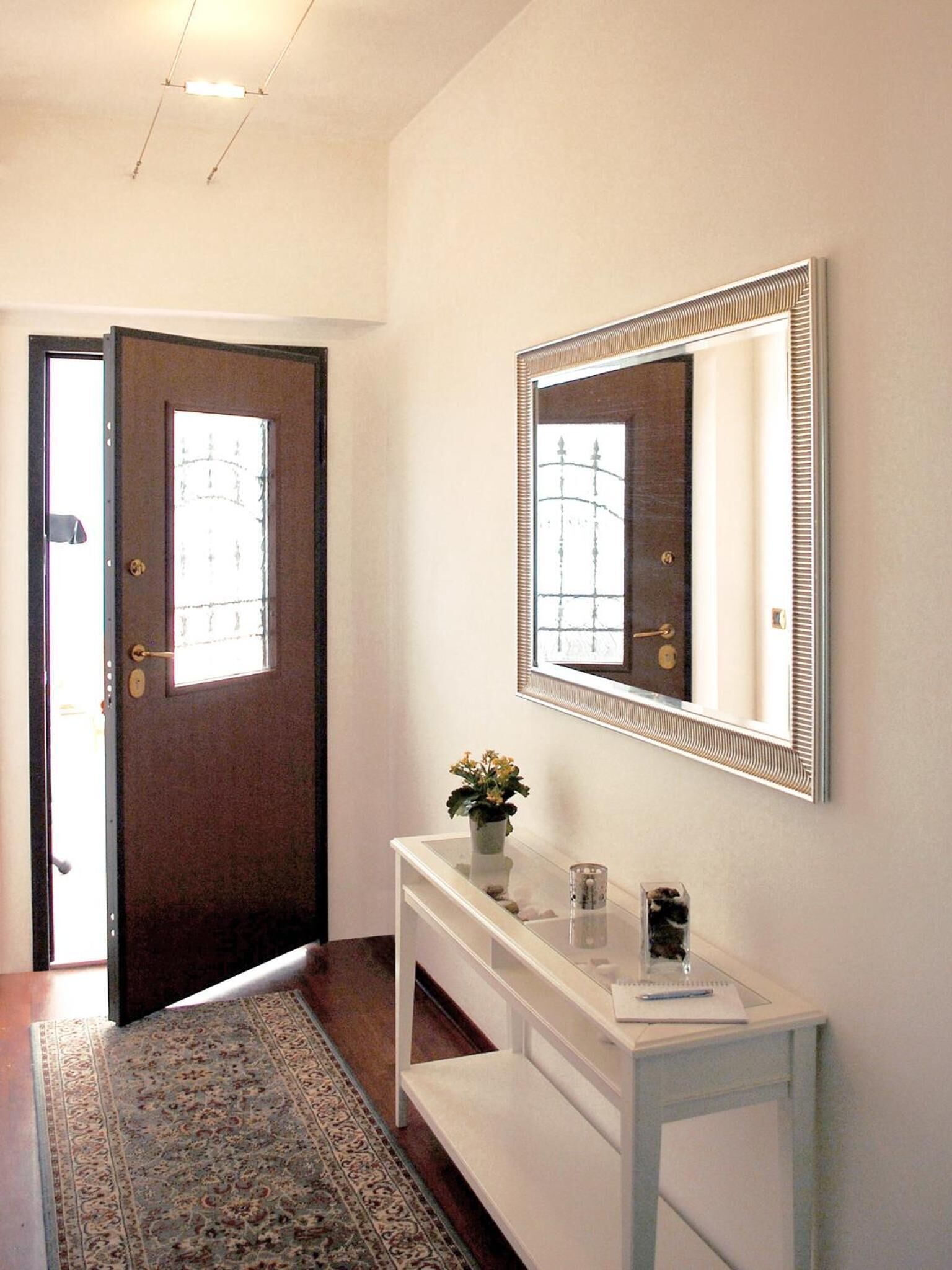 A hallway with a dark wooden door, a white console table with a mirror, and a patterned rug.