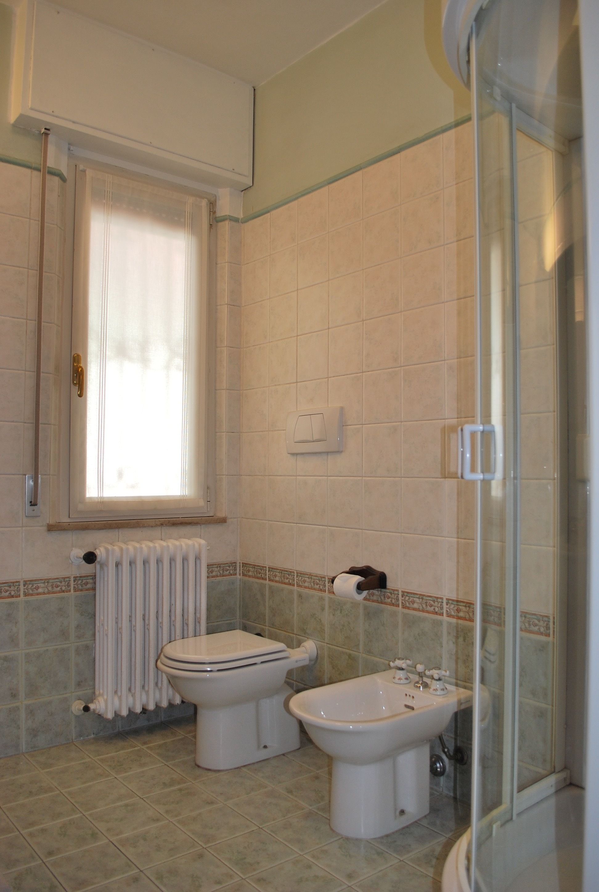 Ein Badezimmer mit Toilette, Bidet und einer Duschkabine aus Glas.