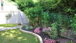 A landscaped garden with a curved stone border, a small tree, and pink flowering plants. - B&B Villa Paradiso (Urbino)
