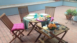 A patio with a table set for a meal, surrounded by chairs, and a small cart with a plant. - B&B Villa Paradiso (Urbino)