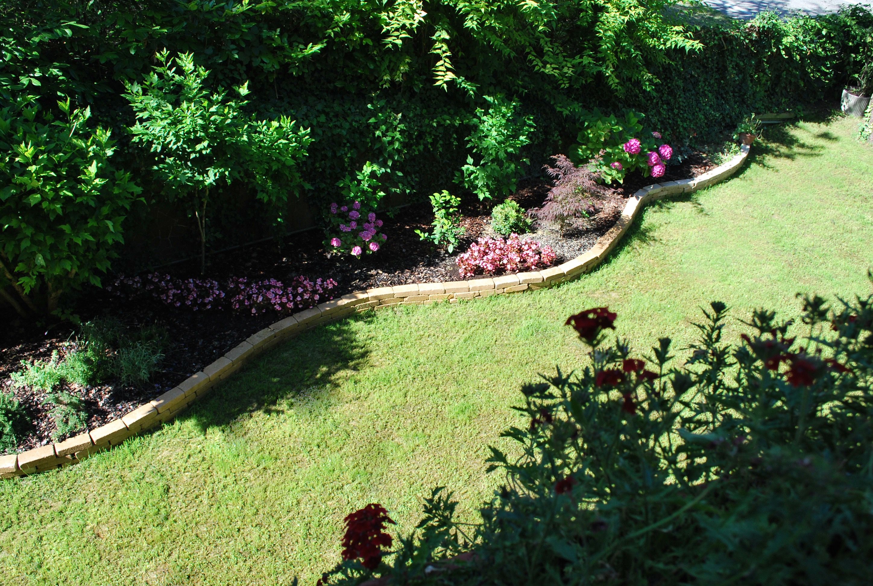 A garden with a curved brick border, various plants, and flowers.