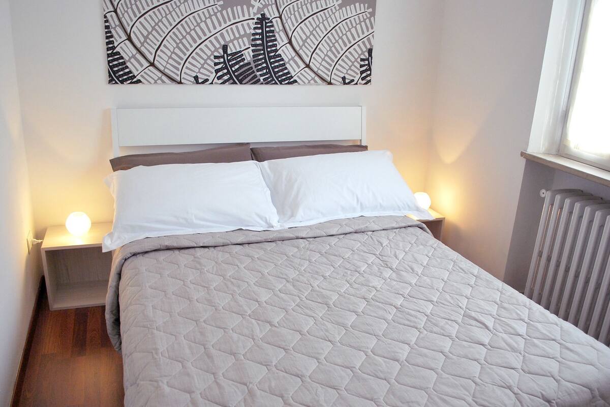 A neatly made bed with a quilted cover, two bedside tables with lamps, and a wall art piece above the bed.
