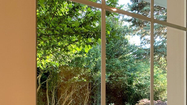 A view through a glass door with a metal handle, leading to a stone pathway surrounded by lush greenery and trees. - B&B Villa Paradiso (Urbino)