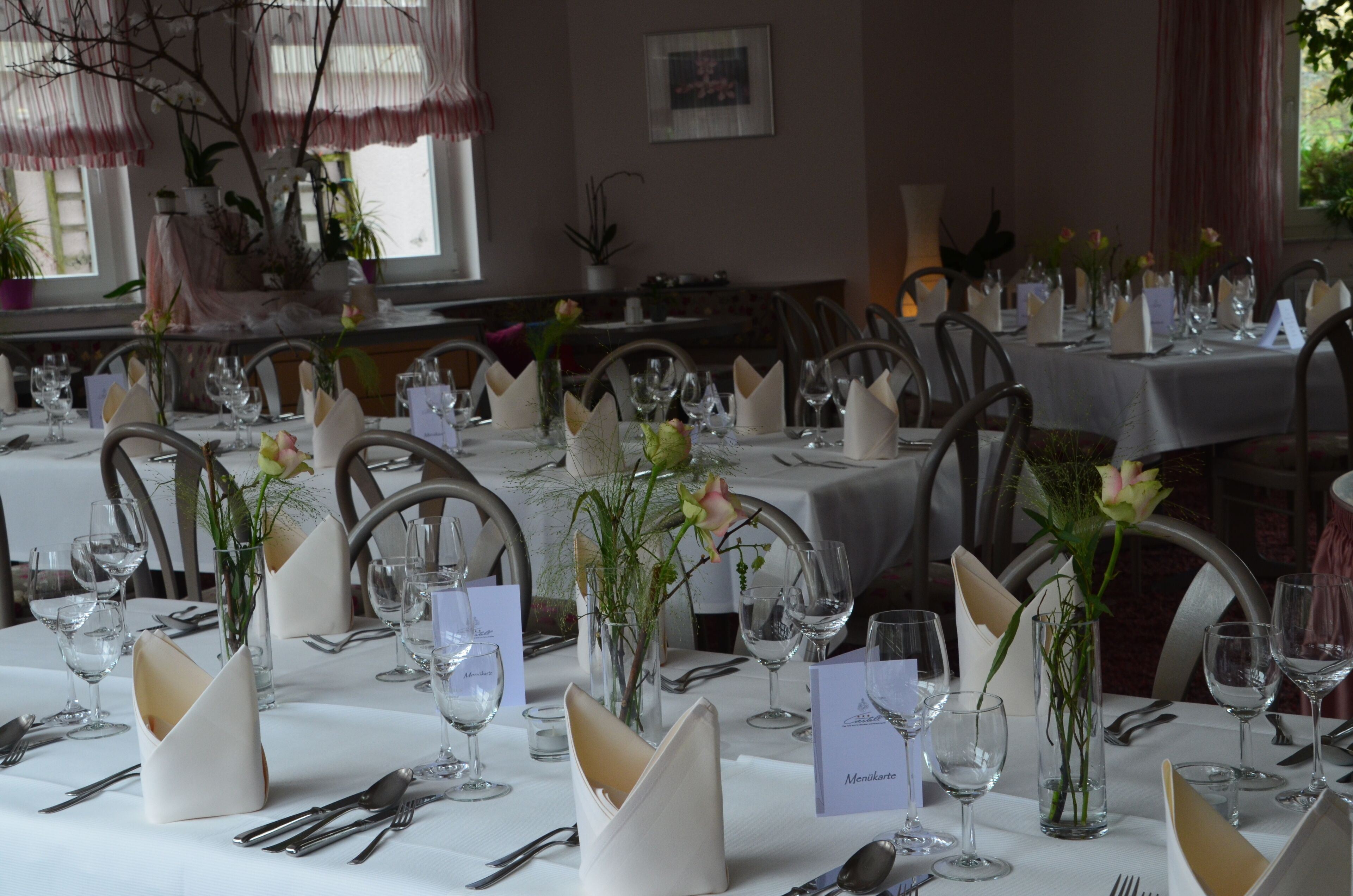 A dining area with multiple tables set for a formal meal, each with place settings, wine glasses, and floral centerpieces.
