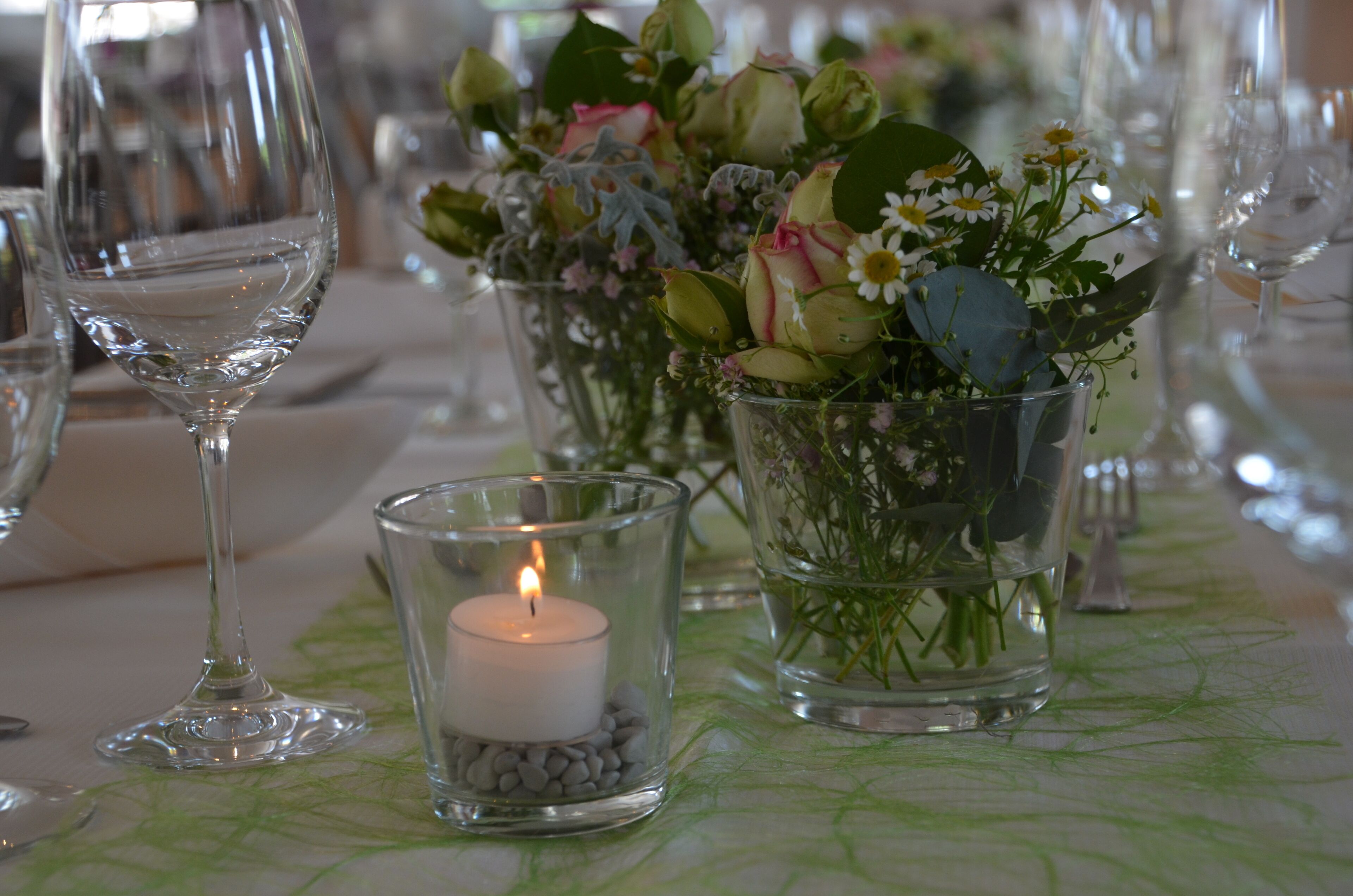 A table with a candle, glass vases with flowers, and wine glasses.