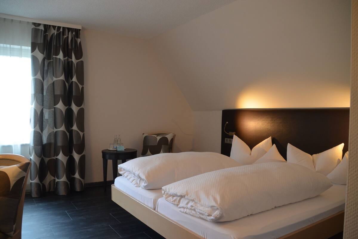 Ein Hotelzimmer mit einem großen Bett, einem Nachttisch, einem Stuhl und einem Vorhang mit geometrischem Muster.