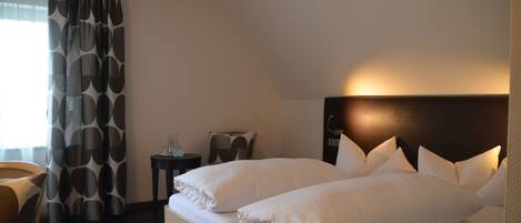 A hotel room with a large bed, a bedside table, a chair, and a curtain with a geometric pattern.
