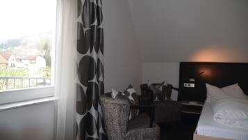 Habitación de hotel con cama, escritorio y una silla. Se ve una ventana con vistas a casas.