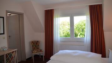 A hotel room with a bed, a chair, a table with glasses, and a window with curtains.