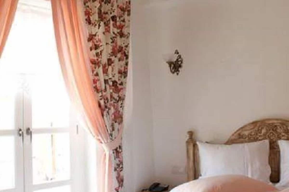 A bedroom with a bed, curtains, a nightstand, and a wall-mounted light.