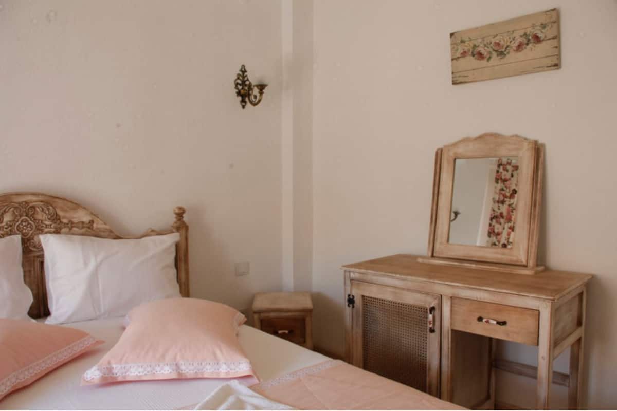A bedroom with a wooden bed, a bedside table, a dresser with a mirror, and a floral wall decoration.