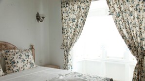 A bedroom with a bed, floral curtains, a nightstand, and a window with a view.