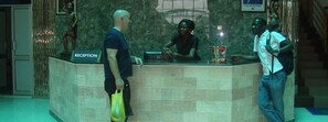 A reception area with a marble counter, a reception sign, and a statue. - Pearl Highway Hotel (Kampala)