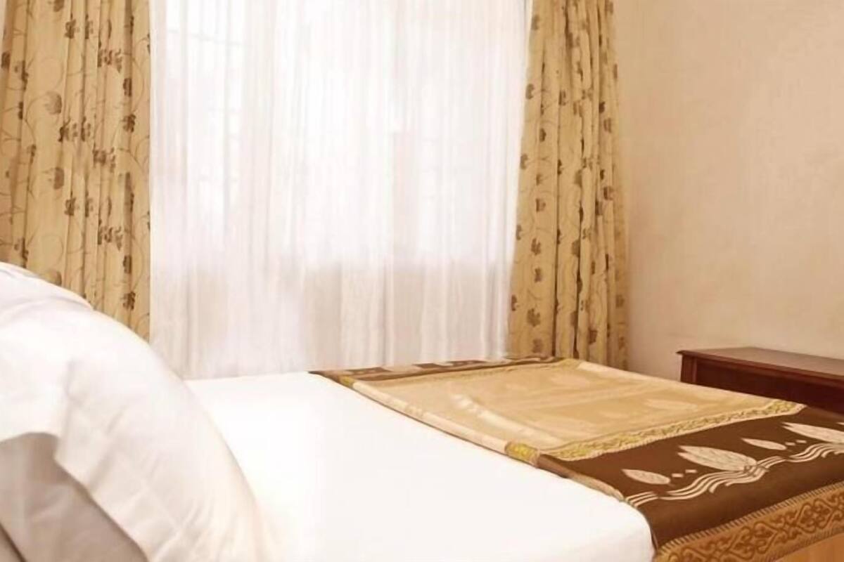 A hotel room with a bed, curtains, and a bedside table.