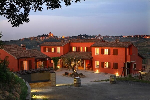 A red villa with multiple rooms, a courtyard, and a view of a hill with buildings in the background.