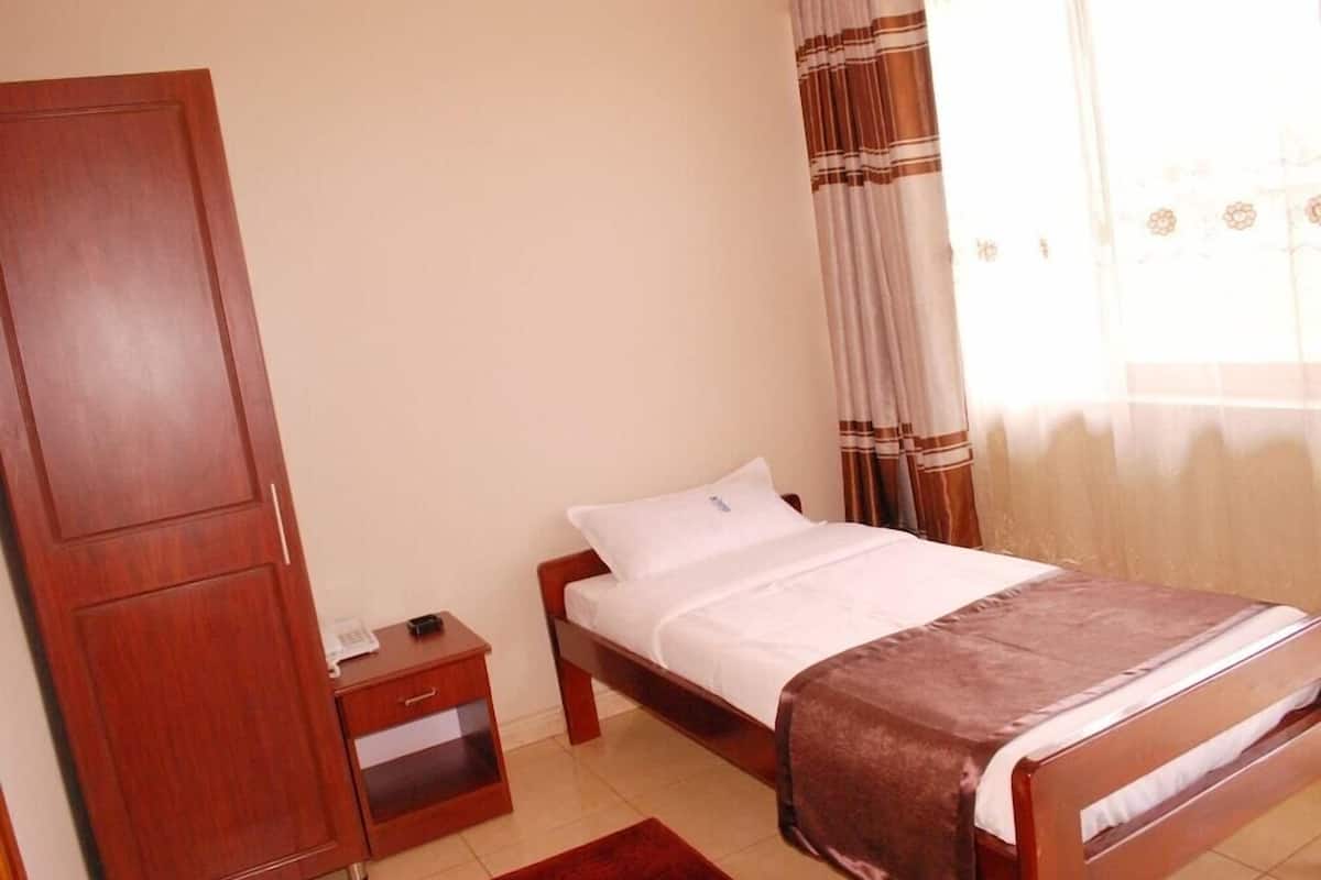 A bedroom with a single bed, a wooden wardrobe, a bedside table, and a window with curtains.
