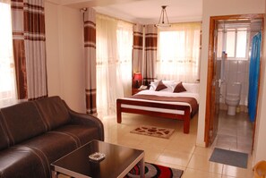 A bedroom with a bed, a sofa, a table, and a bathroom visible through an open door.