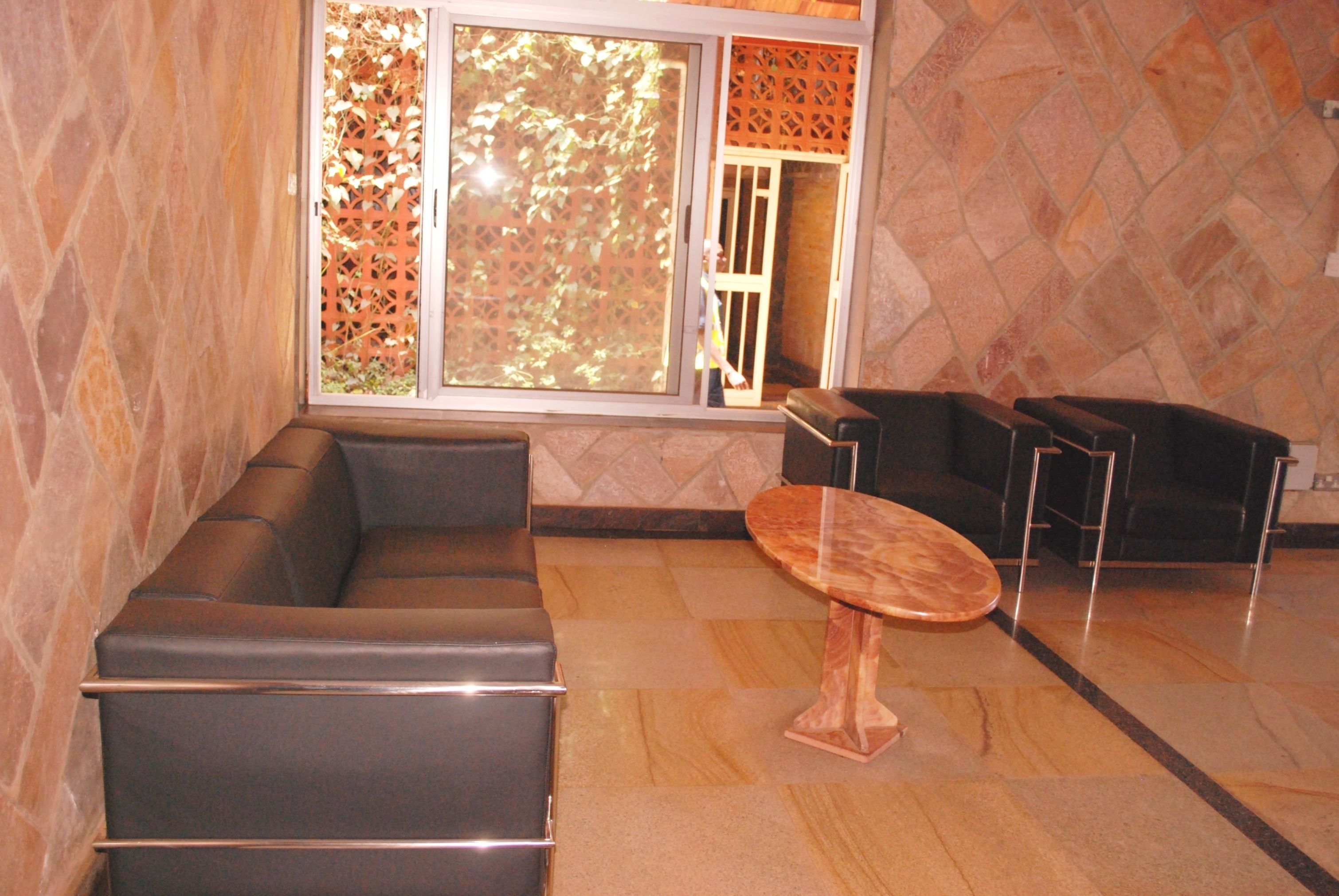 A modern interior with a leather sofa, a round wooden table, and a view through a window with a lattice screen.