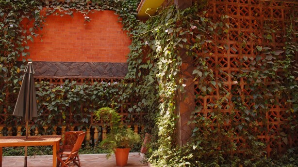 An outdoor patio with a brick wall, a wooden table, and chairs. - Seb Hotel (Kampala)