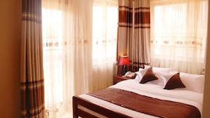A hotel room with a bed, curtains, a nightstand, and a lamp. - Seb Hotel (Kampala)