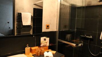 Une salle de bain moderne avec une baignoire noire, une douche en verre et une petite table en bois sur laquelle sont posées des serviettes et des articles de toilette.