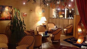 A cozy lounge area with comfortable seating, a table with a lamp, and a large plant.